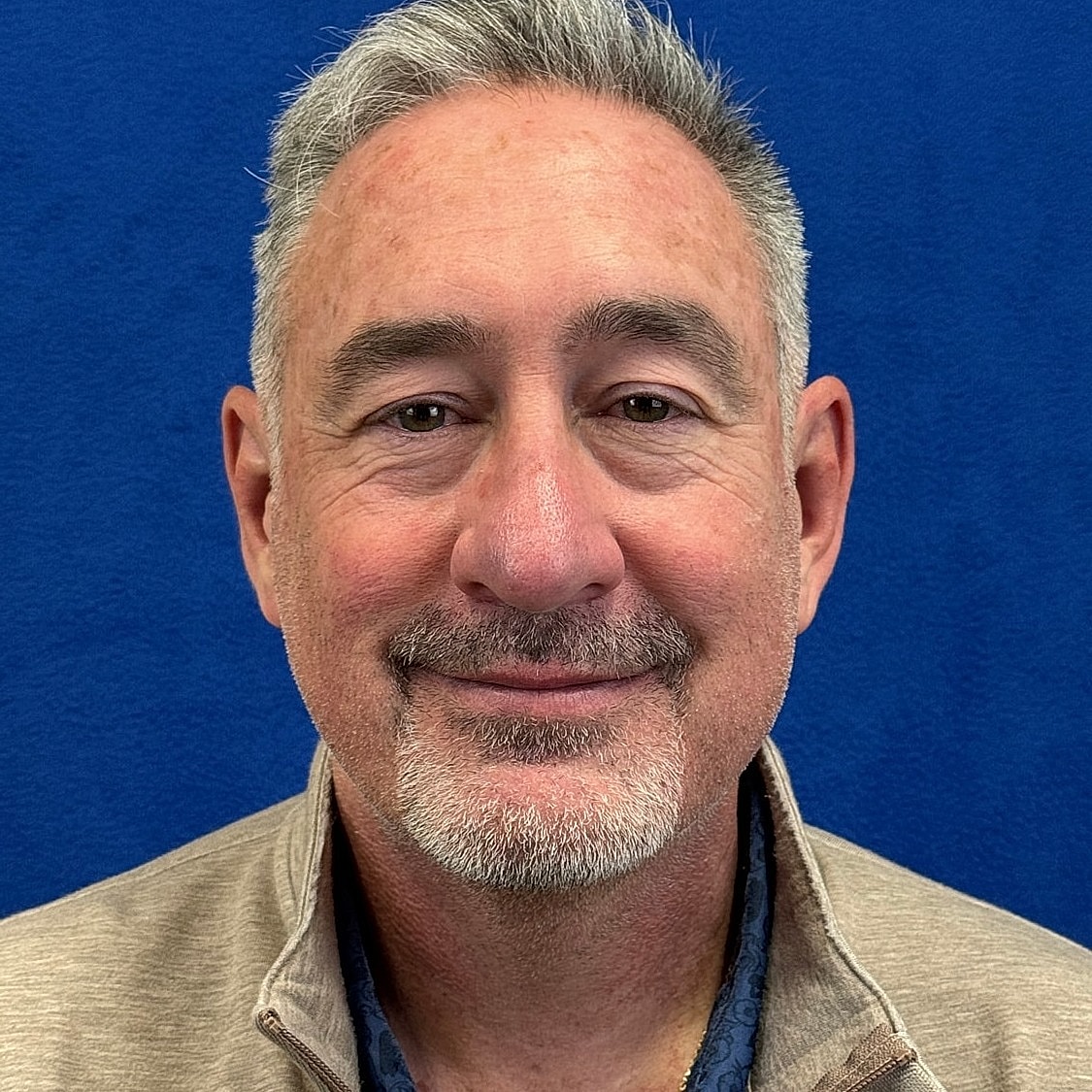 Smiling man in a beige jacket, blue background.