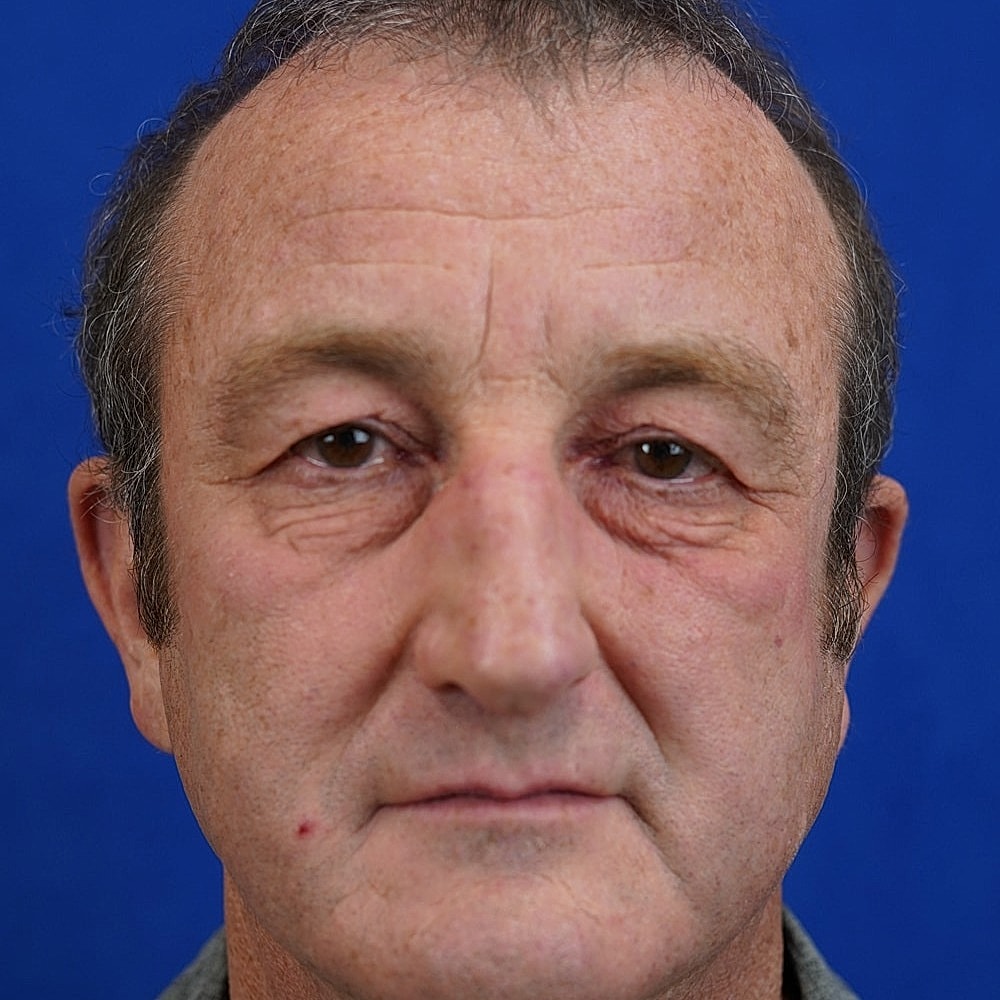 Middle-aged man with neutral expression and blue background.